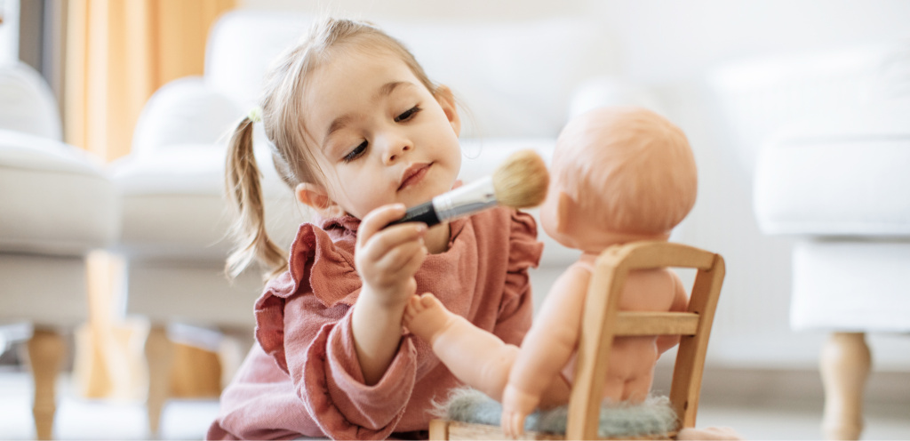 Девочка двух лет играет с кисточкой и куклой — проявление самостоятельности в период кризиса двухлеток