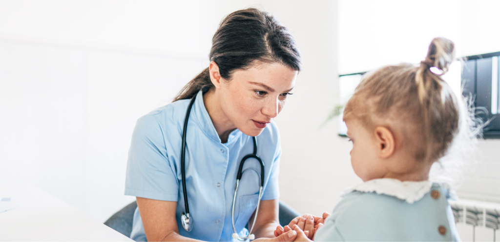 Врач проводит консультацию и осмотр двухлетней девочки во время плановой диспансеризации